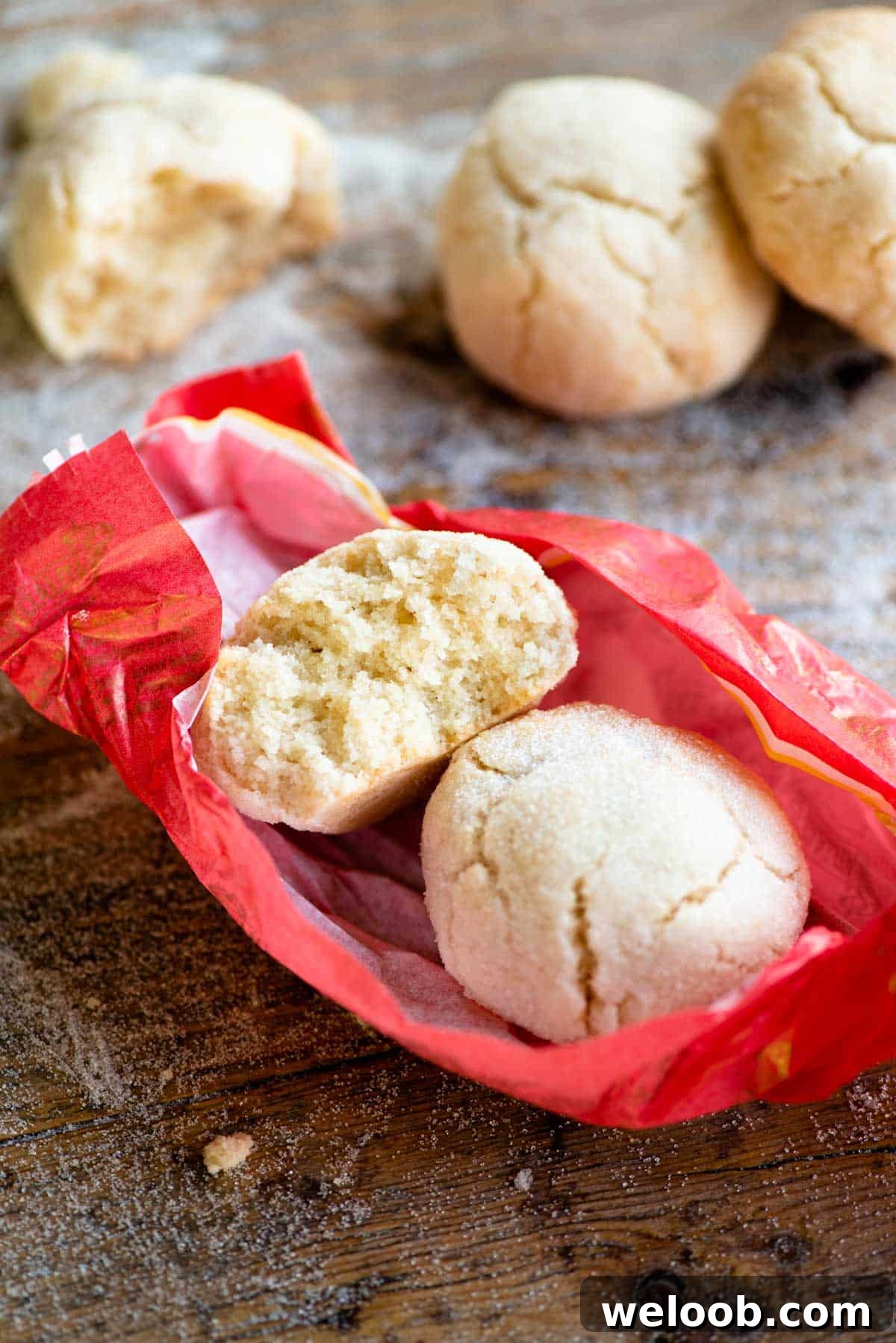 A close up of two amaretti cookies in a pink wrapper, one cut in half to see the texture inside.