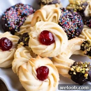 A close up of Italian butter cookies on a plate. In the centre is a round cookie with a candied cherry on top.