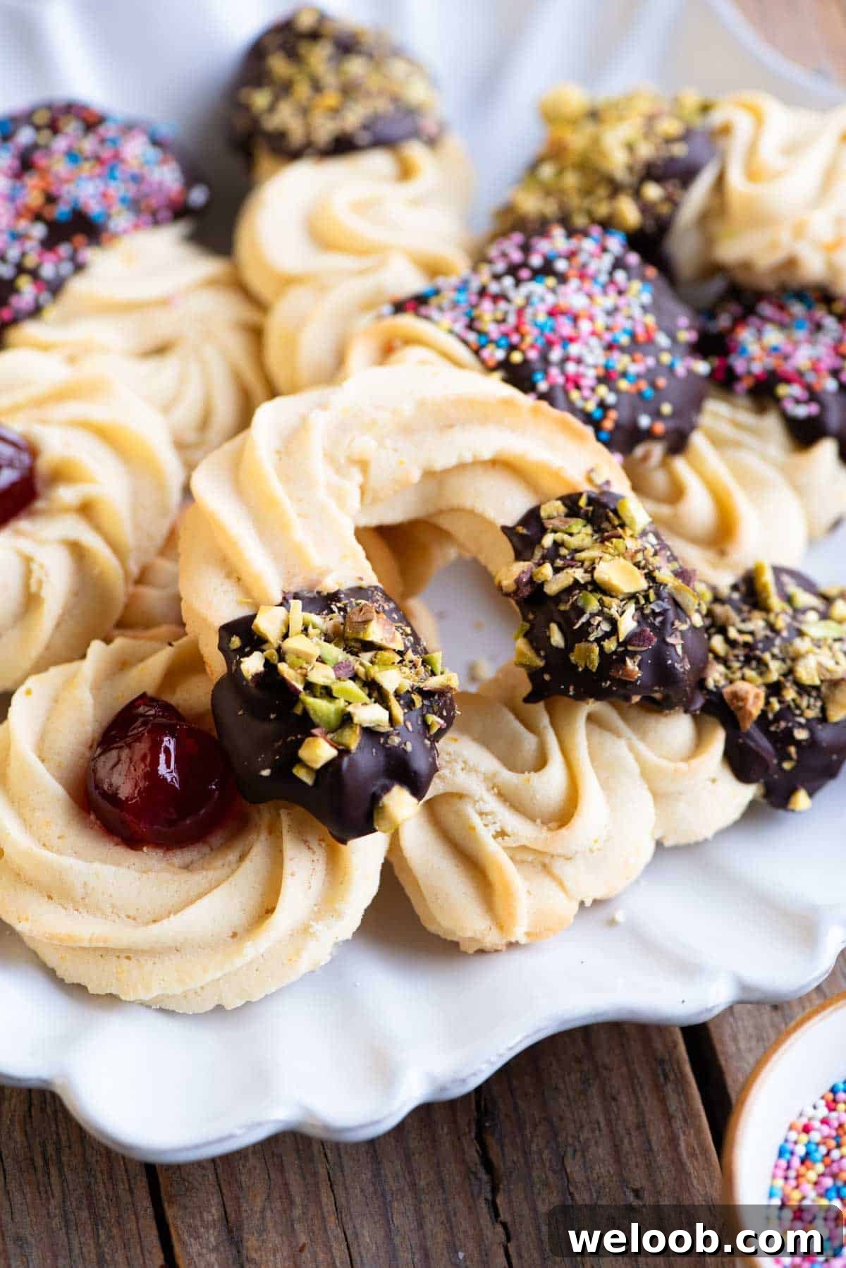 A close up of Italian butter cookies on a plate some half dipped in chocolate and sprinkled with pistachios.