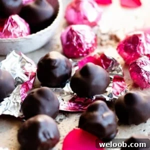 A close up cropped image of homemade baci chocolates in pink foils on a travertine worktop.