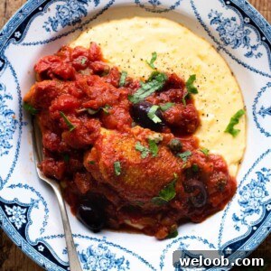 A cropped close up of chicken puttanesca with creamy polenta in a blue bowl.