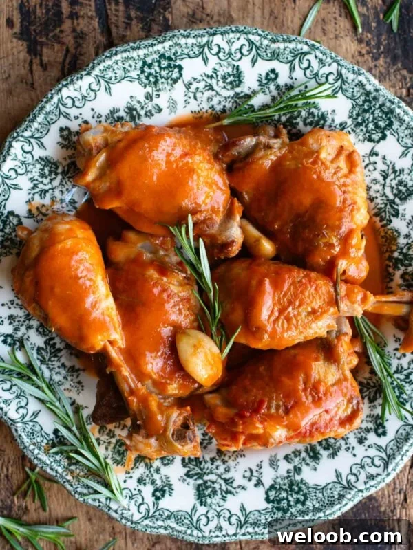 An overhead shot of chicken thighs and drumsticks on a green patterned plate with rosemary and garlic.