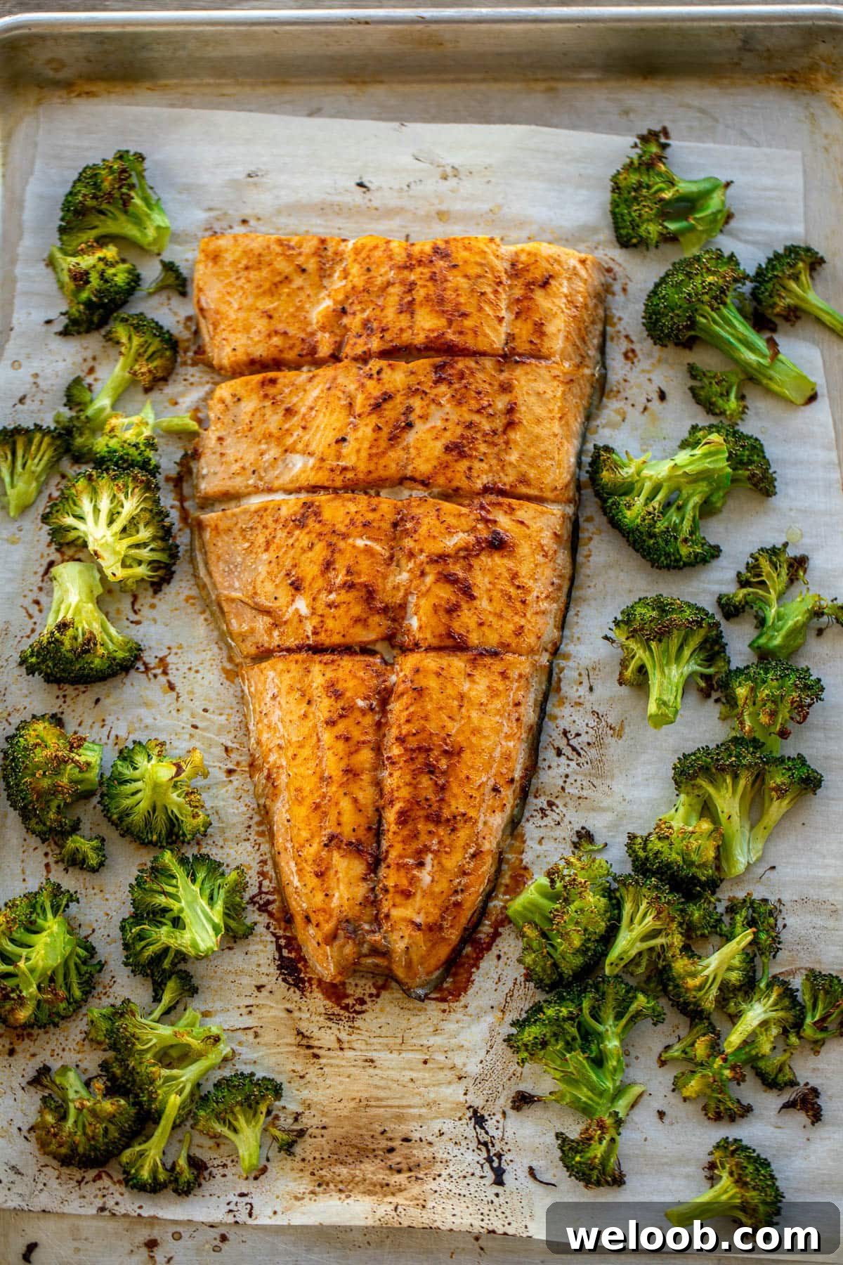 Large salmon fillet and roasted broccoli on a sheet pan
