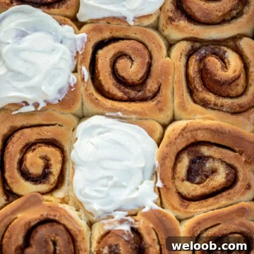 Cinnamon rolls in a pan, some of the rolls frosted with cream cheese frosting
