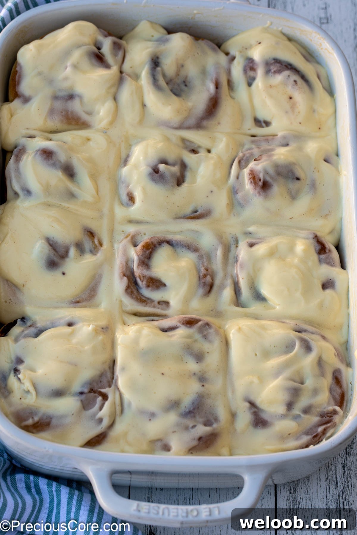 Cinnamon Rolls completely covered with cream cheese frosting in a white baking dish.