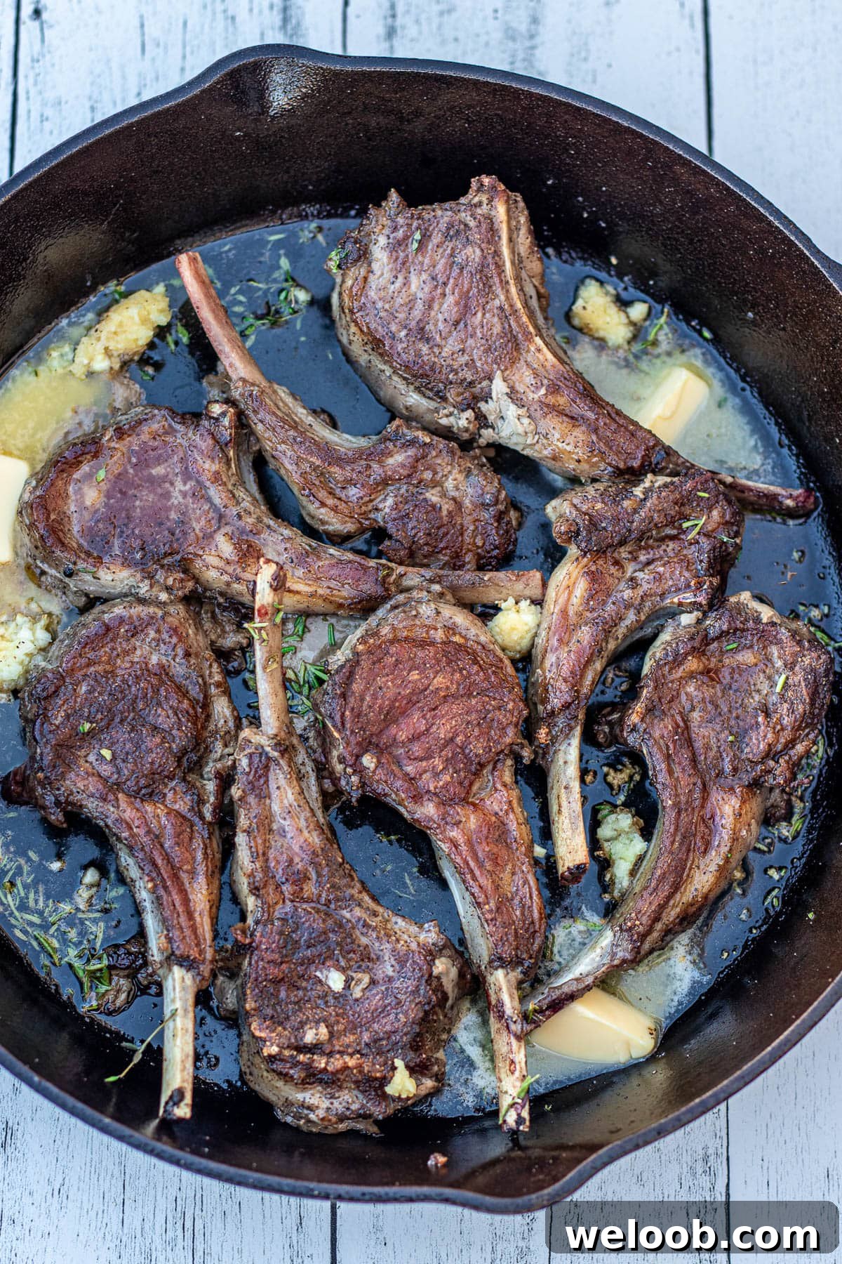 Flipped lamb chops with butter and garlic in pan.