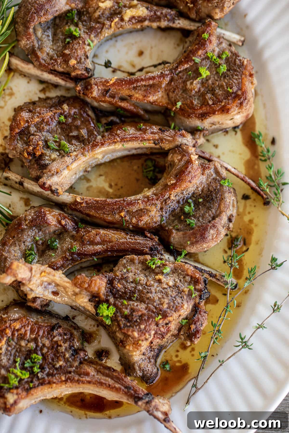 Pan seared lamb chops served on a large tray, garnished with fresh thyme and rosemary leaves