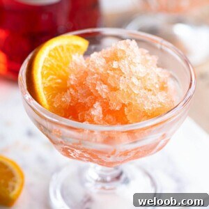 A close up on Aperol Spritz Granita in a small glass bowl with an orange wedge.