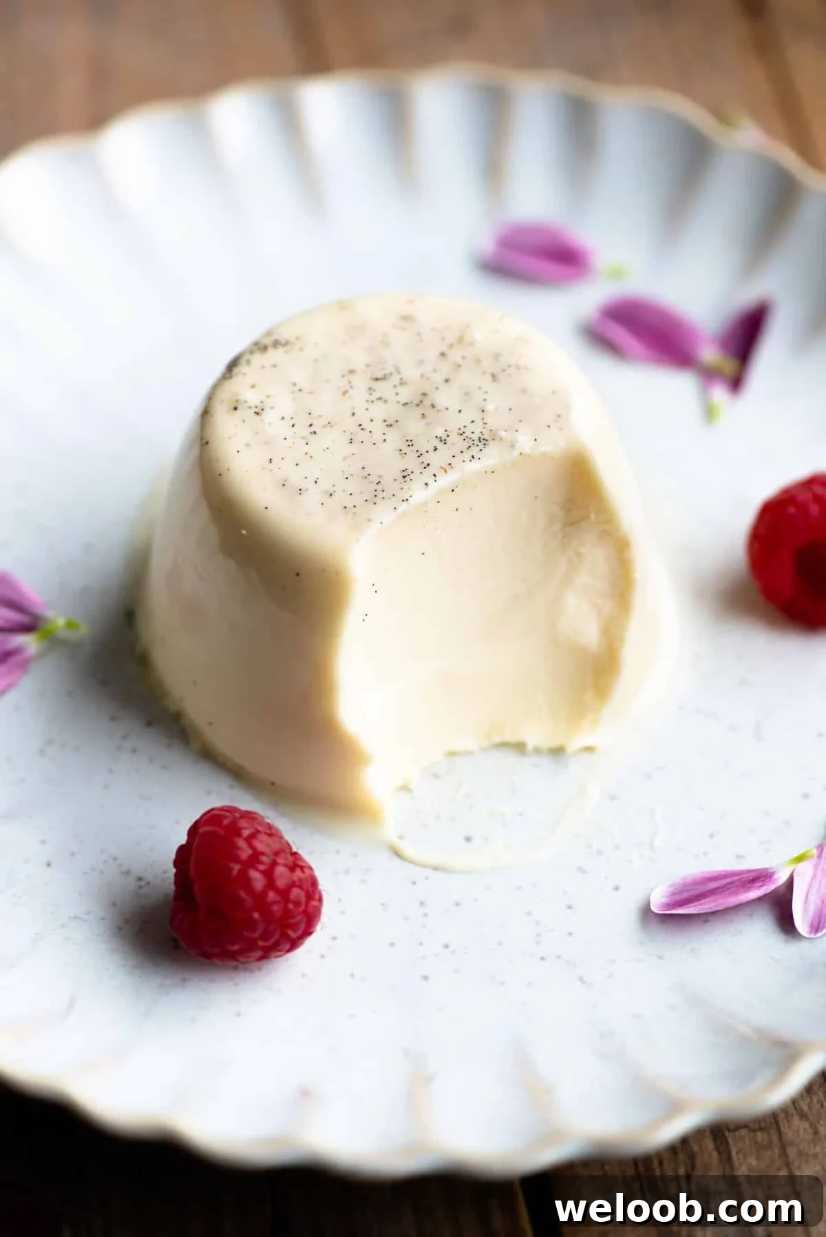 A vanilla panna cotta on a plate with a bite out and raspberries at the side.