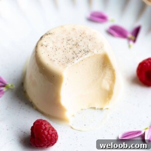 A close up of a vanilla panna cotta on a white plate with raspberries at the side.