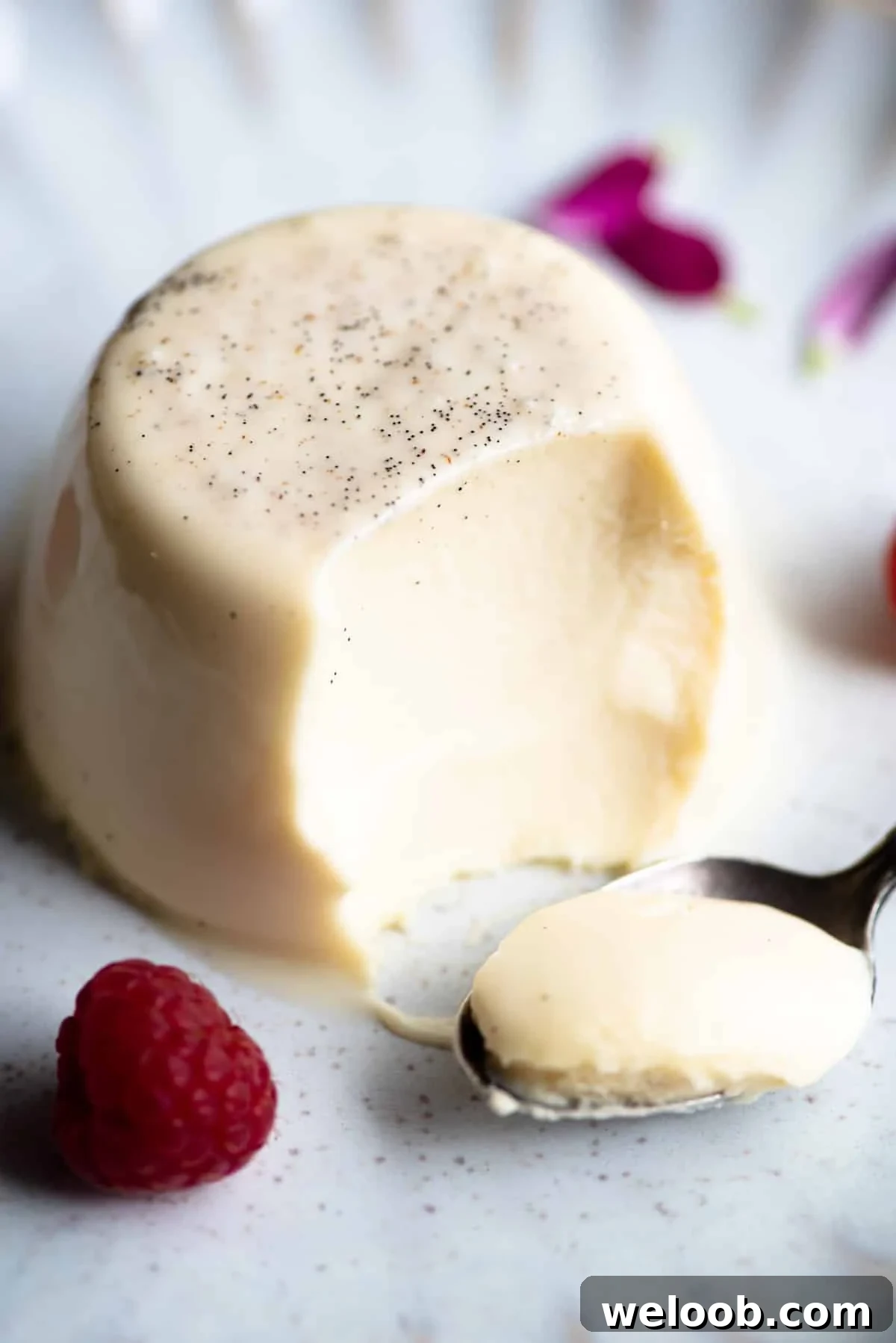 A close up of a vanilla panna cotta with a bite out and spoon at the side.