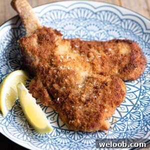 A cropped square image of Veal Milanese on a blue plate with a lemon wedge at the side.