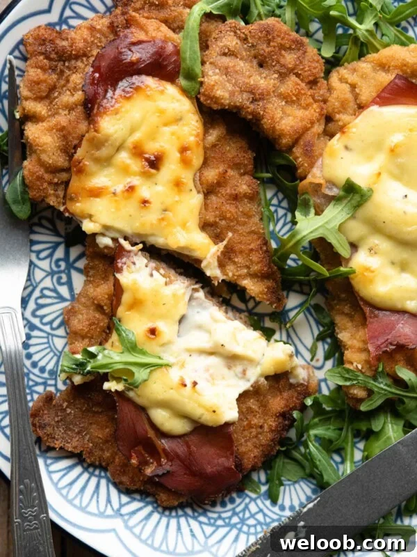 A close up of a veal cutlet cut in half with parmesan cream and prosciutto on top