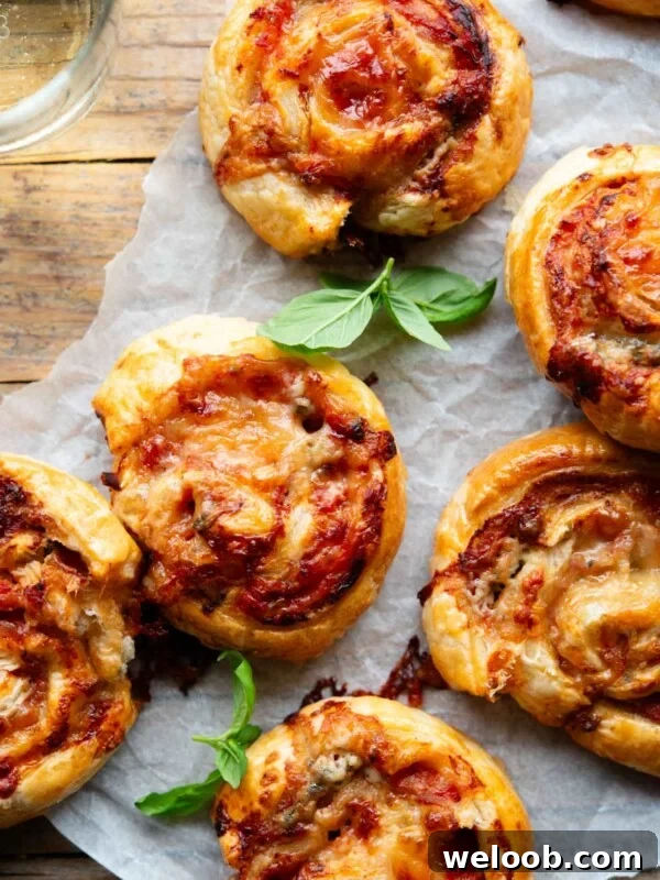 An overhead shot of pizza pinwheels on a wooden board with a basil leaf and glass of wine at the side.