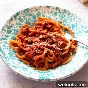 A cropped square image of Tuscan sausage pasta in a blue speckled bowl.