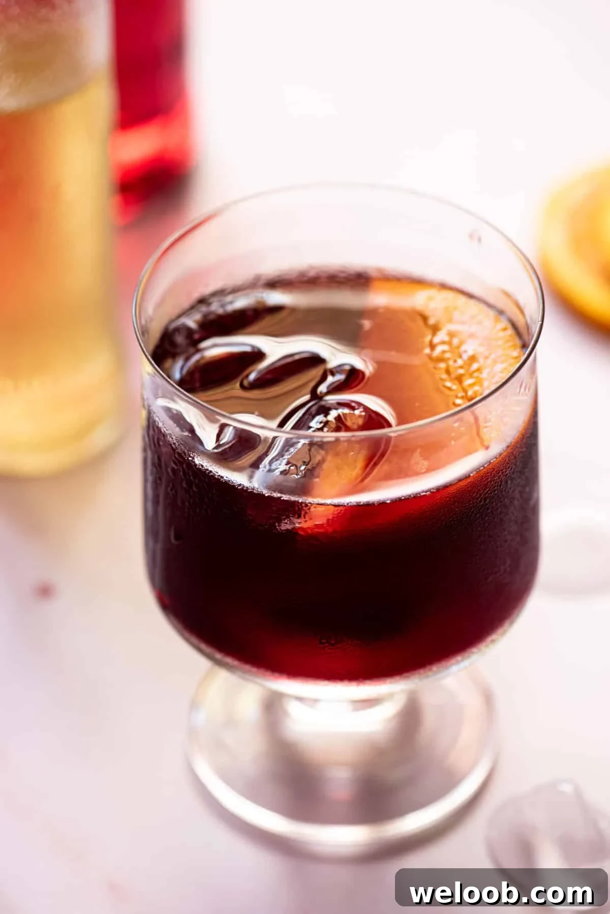 A close up of a red wine spritz in a glass with a slice of orange.