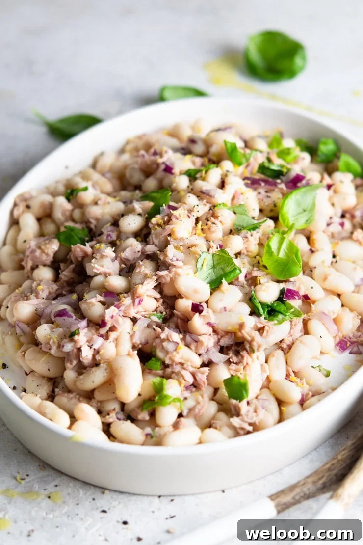 A side shot of a white bean salad with tuna and basil on a white serving plate