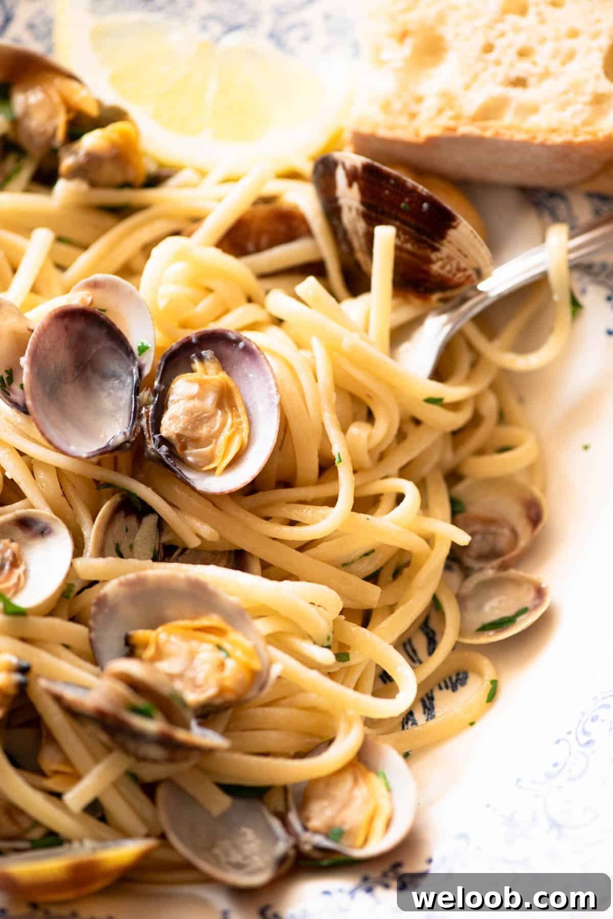 A close up of linguine pasta with clams, parsley and lemon in a bowl.