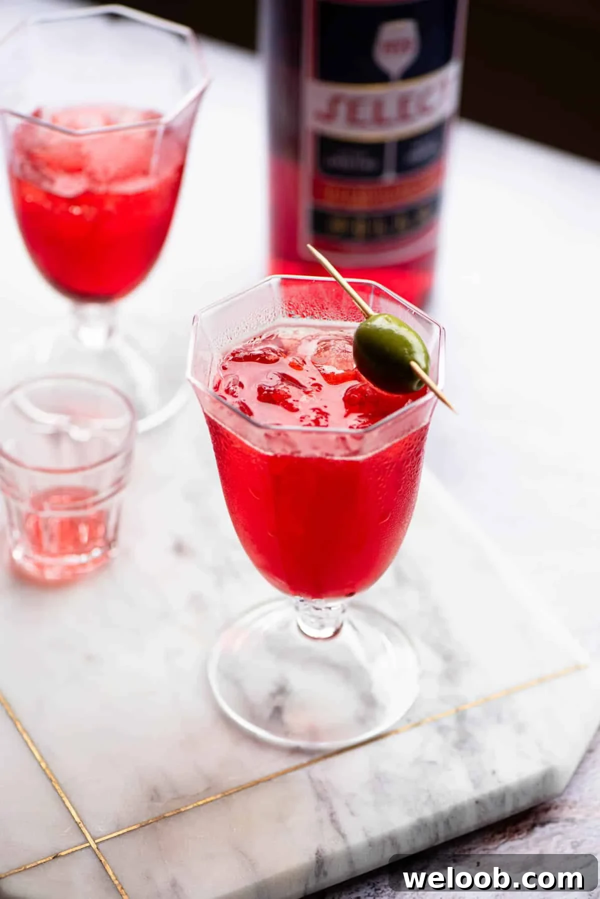 A select spritz in a glass topped with an olive.