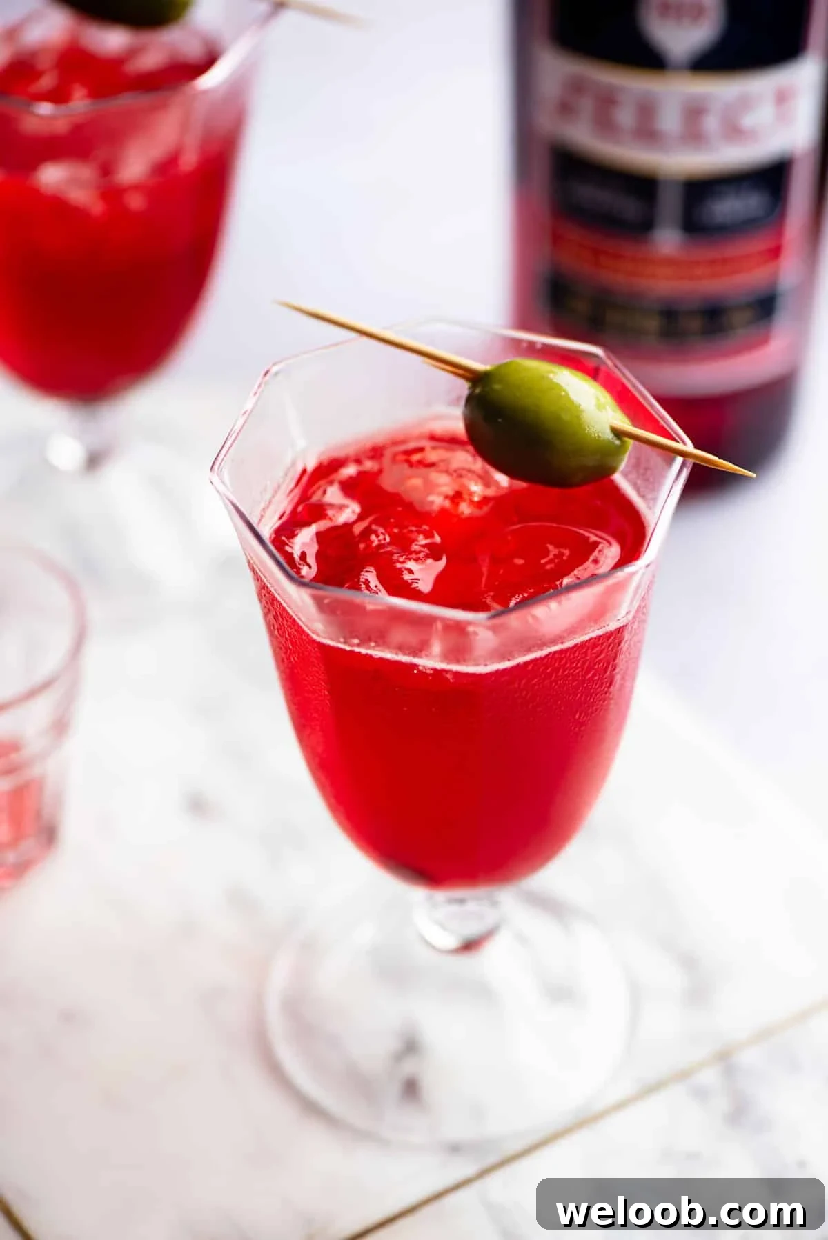 A close up of a Venetian Select Spritz on a marble chopping board topped with an olive.