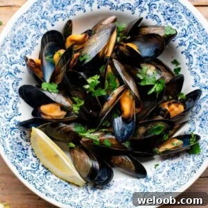 A cropped image of mussels in a blue bowl topped with fresh parsley and lemon.
