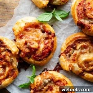 A close up overhead shot of pizza pinwheels on a sheet of baking parchment with basil leaves.