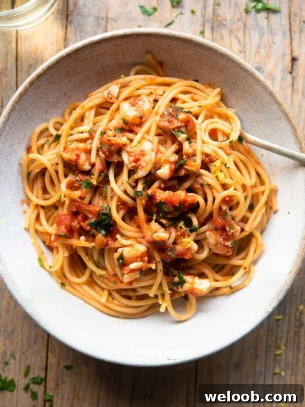 An overhead shot of shrimp spaghetti in a rustic bowl sitting on a wooden surface with a glass of white wine at the side.