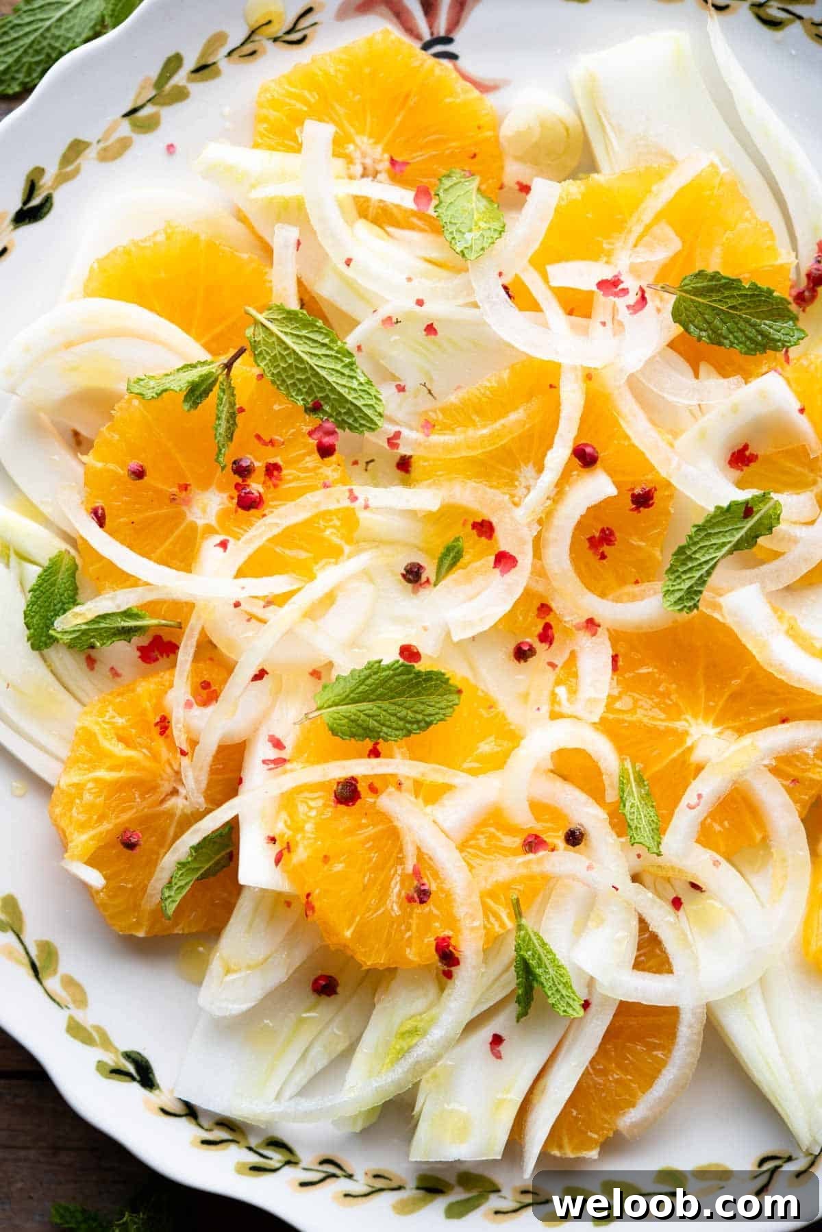 A close up of a fennel orange salad with white onion, mint leaves and pink peppercorns.