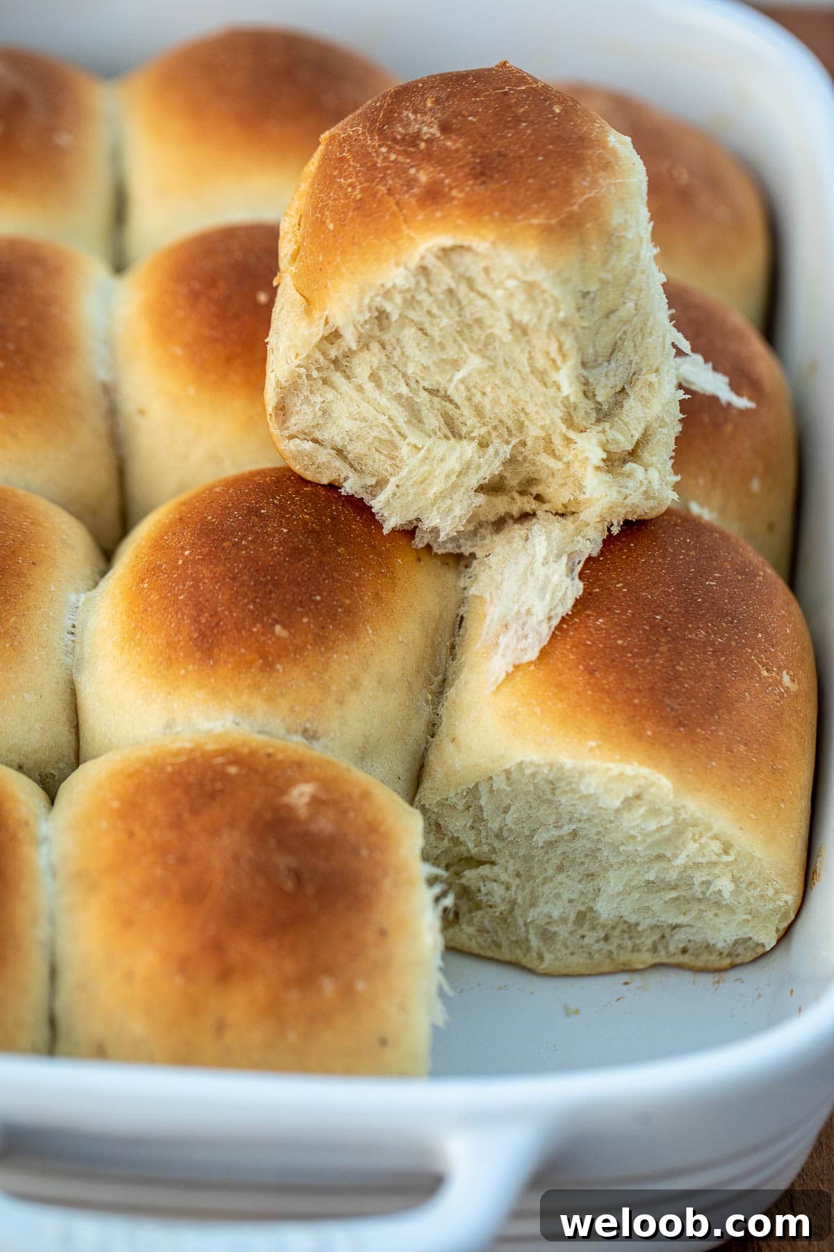 Banana bread rolls in pan with one bread roll on top showing fluffiness