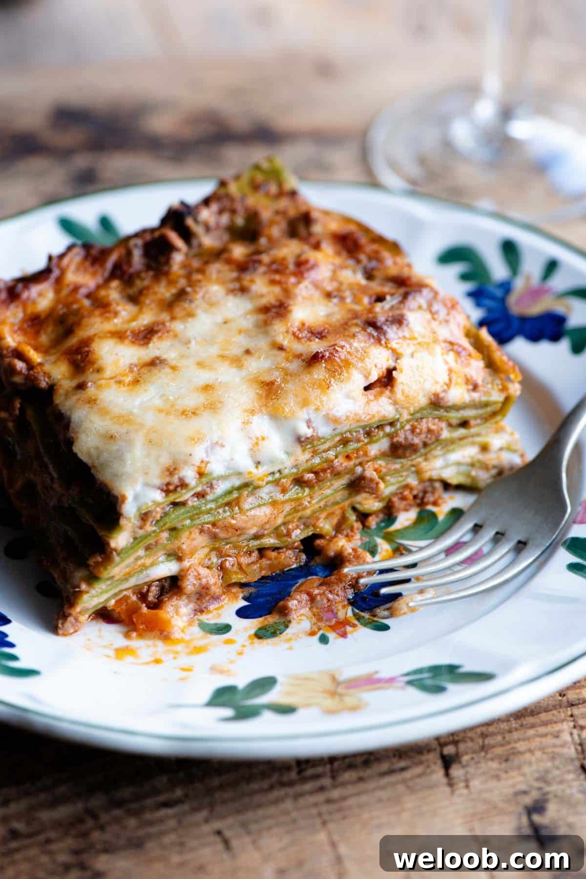 A close up of a slice of Lasagna Bolognese on a plate with a flower pattern.