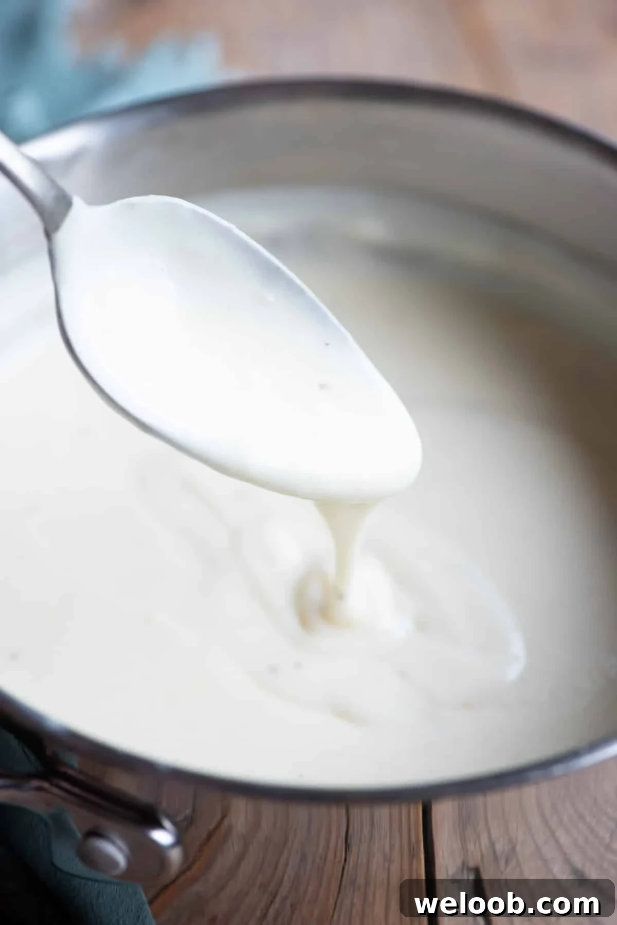 A close up of Italian Besciamella sauce in a pot with some dripping off a spoon.