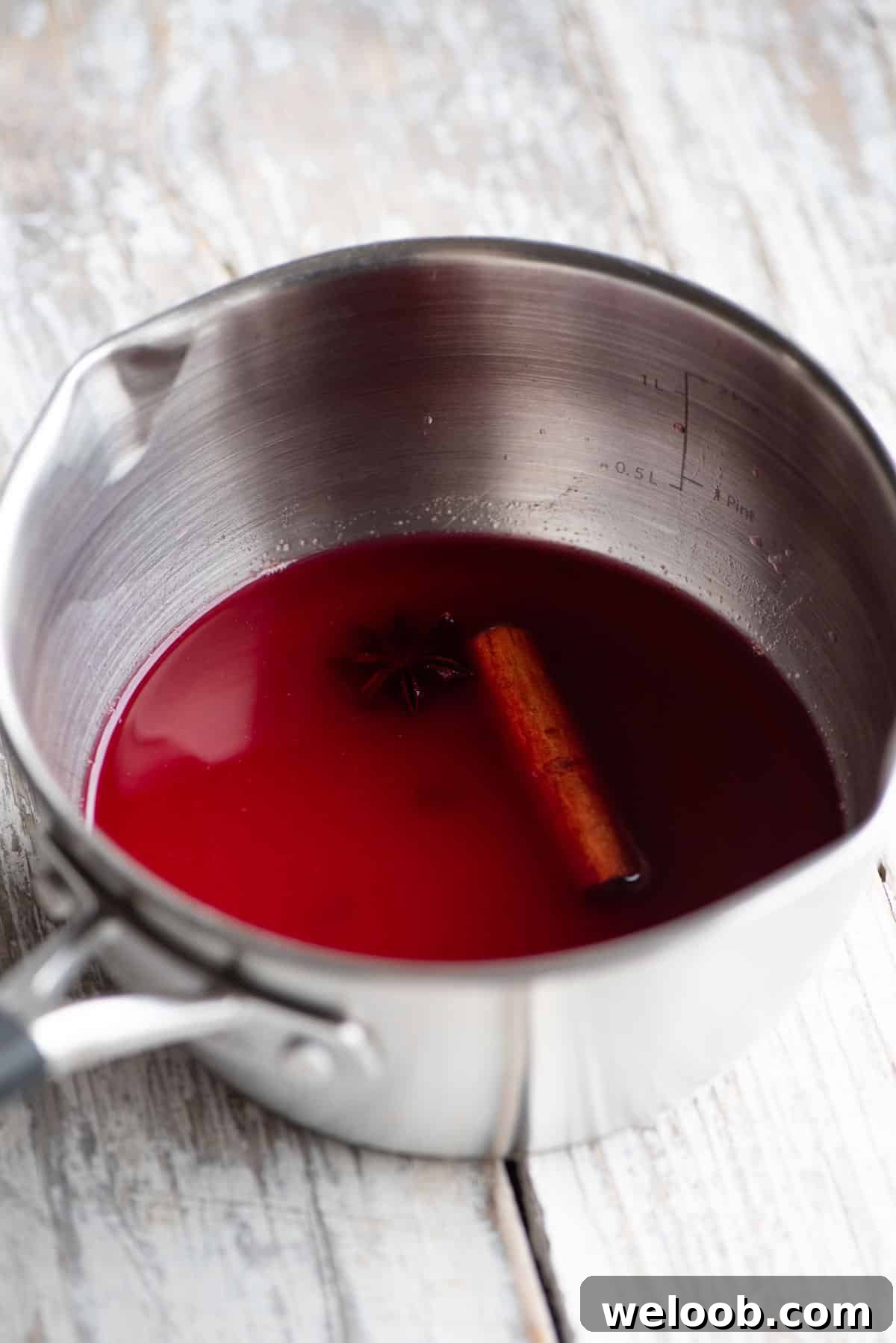 A small pot with cranberry juice and Christmas spices inside sitting on a white wooden table.