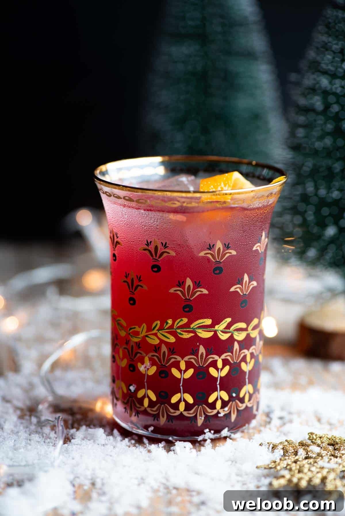 A close up side shot of a Cranberry and Prosecco cocktail sitting on a wooden table with snow all around.