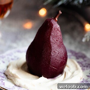 A close up of a red wine poached pear on top of amaretto whipped cream on a small dessert plate.