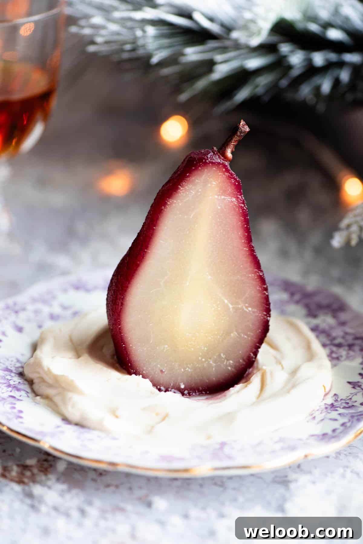 A red wine poached pear cut in half on a plate with Amaretto whipped cream, the background is Christmassy.
