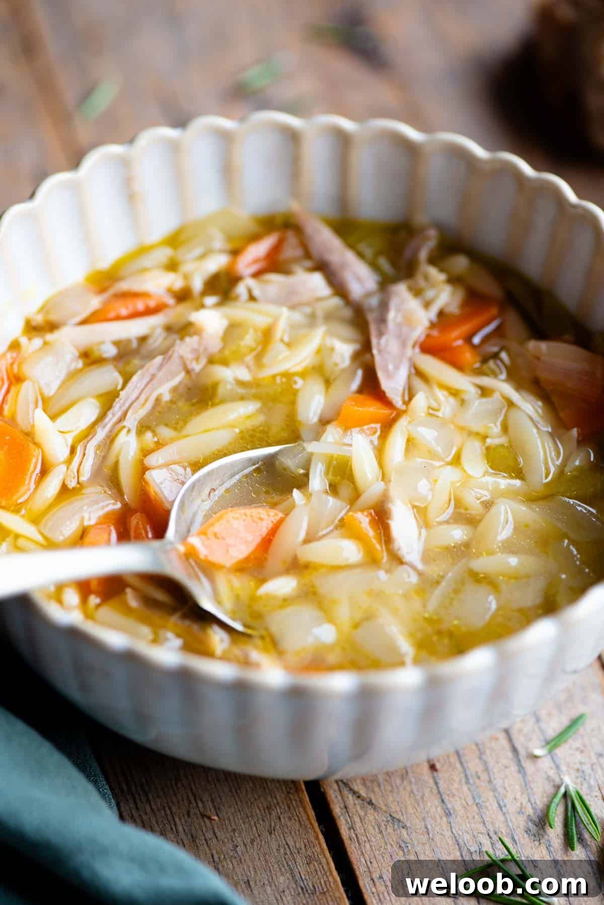 A close up side shot of lemon chicken orzo soup in a bowl with a spoon.