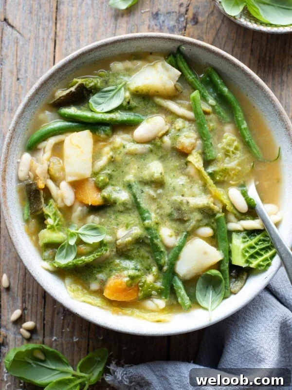 An overhead shot of a bowl of Ligurian minestrone with lots of vegetables and basil pesto sitting on a wooden background