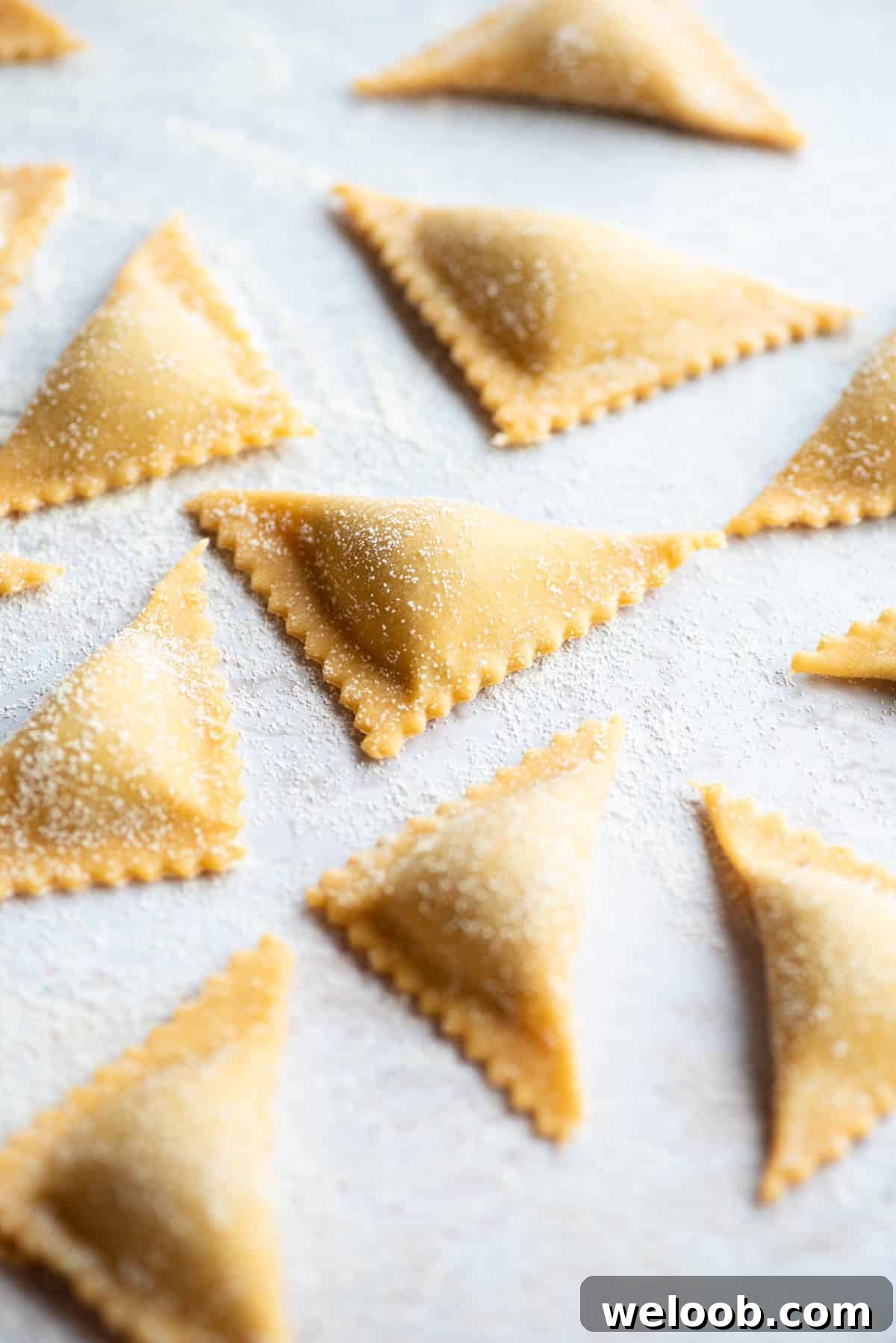 A close up side shot of fresh Triangoli pasta on a light grey coloured board.