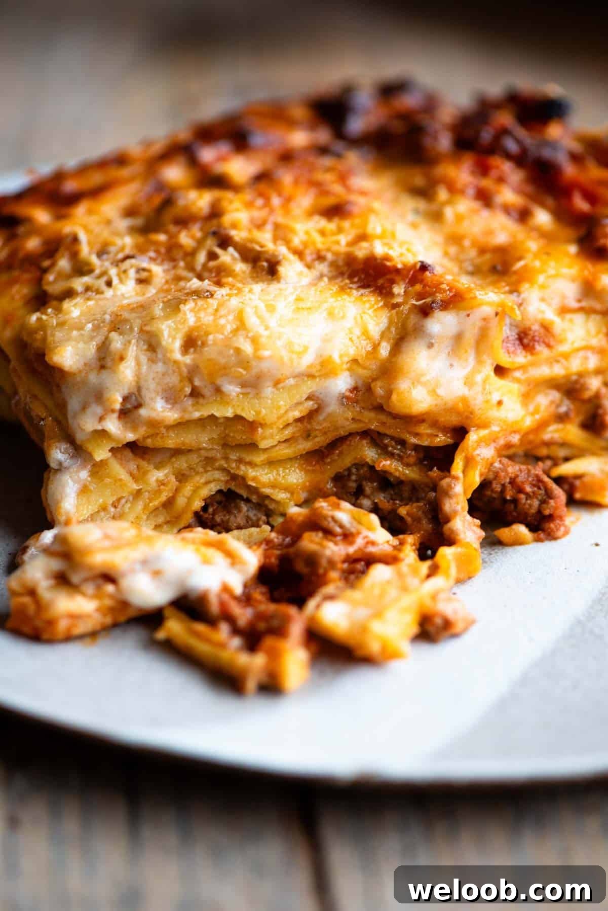 One slice of lamb lasagna on a plate sitting on a wooden surface.