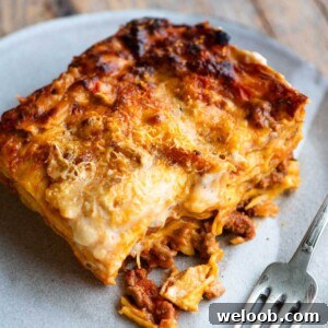 A close up of a slice of lamb lasagna on a plate with a fork at the side.