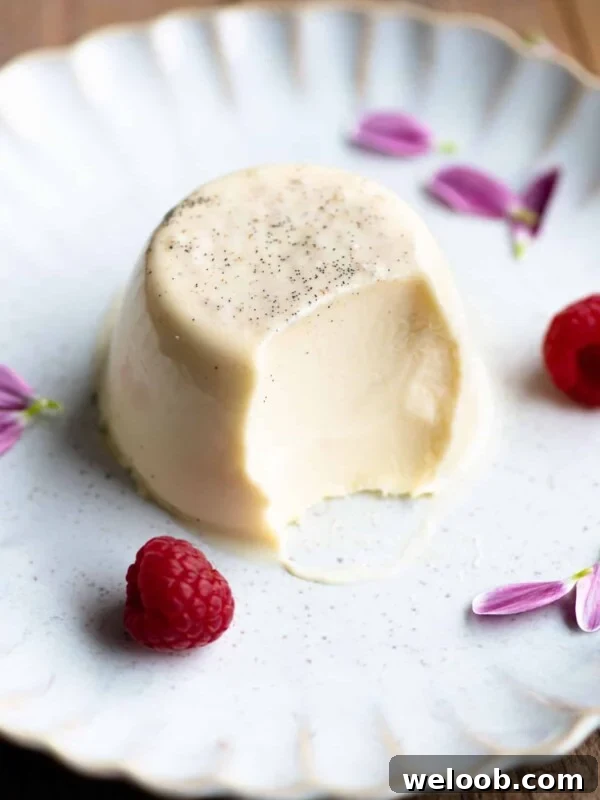A vanilla panna cotta on a plate with a bite out and raspberries at the side.