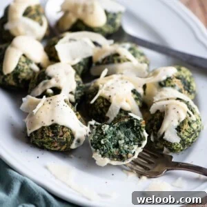 A close up of spinach balls on a white serving plate drizzled with Parmigiano cream.