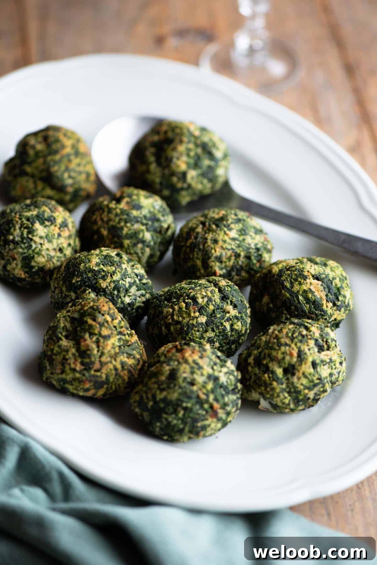Baked spinach balls on a white serving plate with a serving spoon.