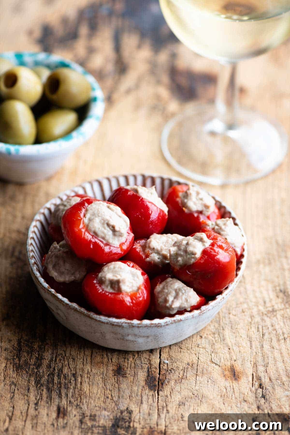 Tuna stuffed cherry peppers in a small dish with olives and a glass of wine at the side.