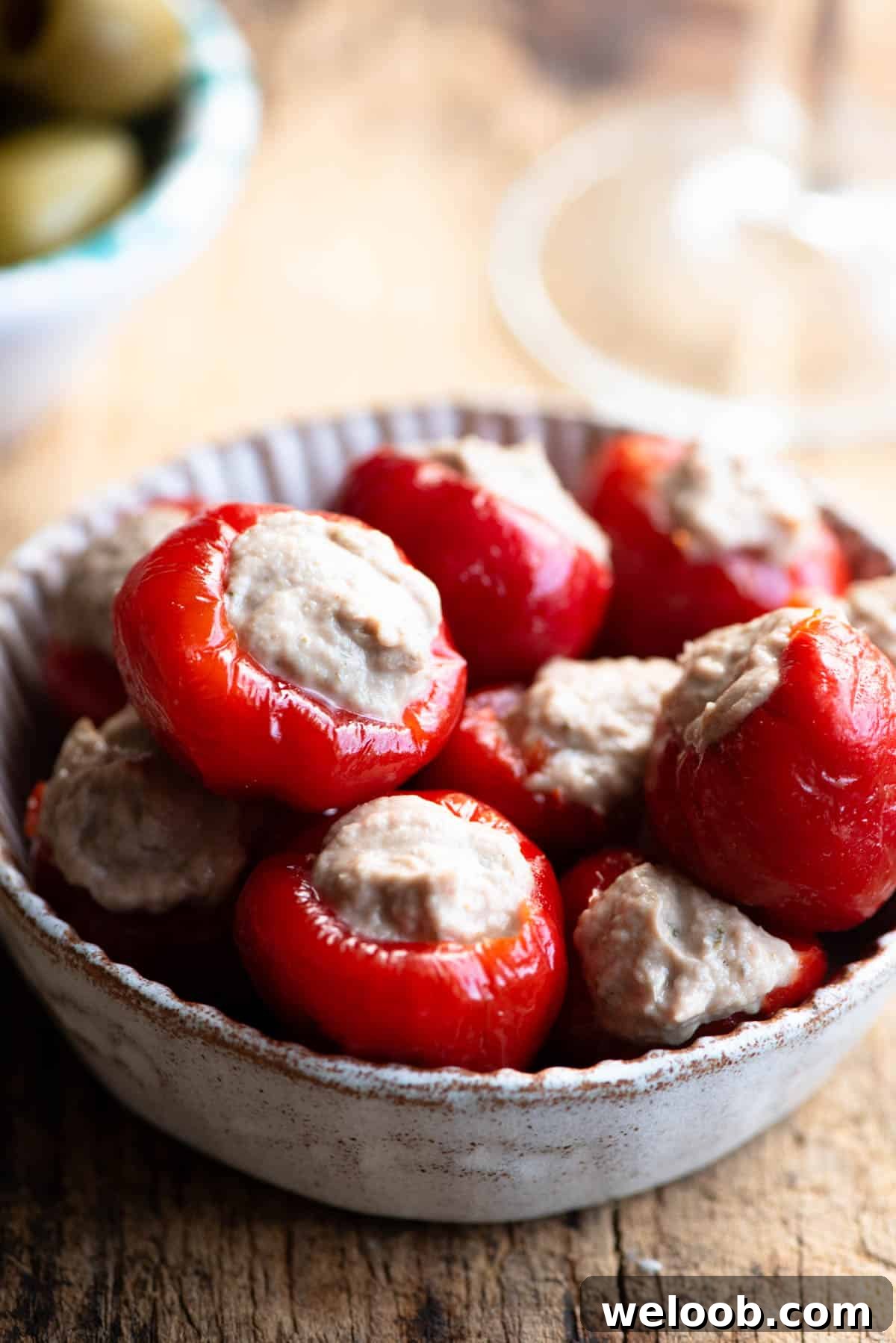 A close up of tuna stuffed cherry peppers in a small dish sitting on a wooden surface.