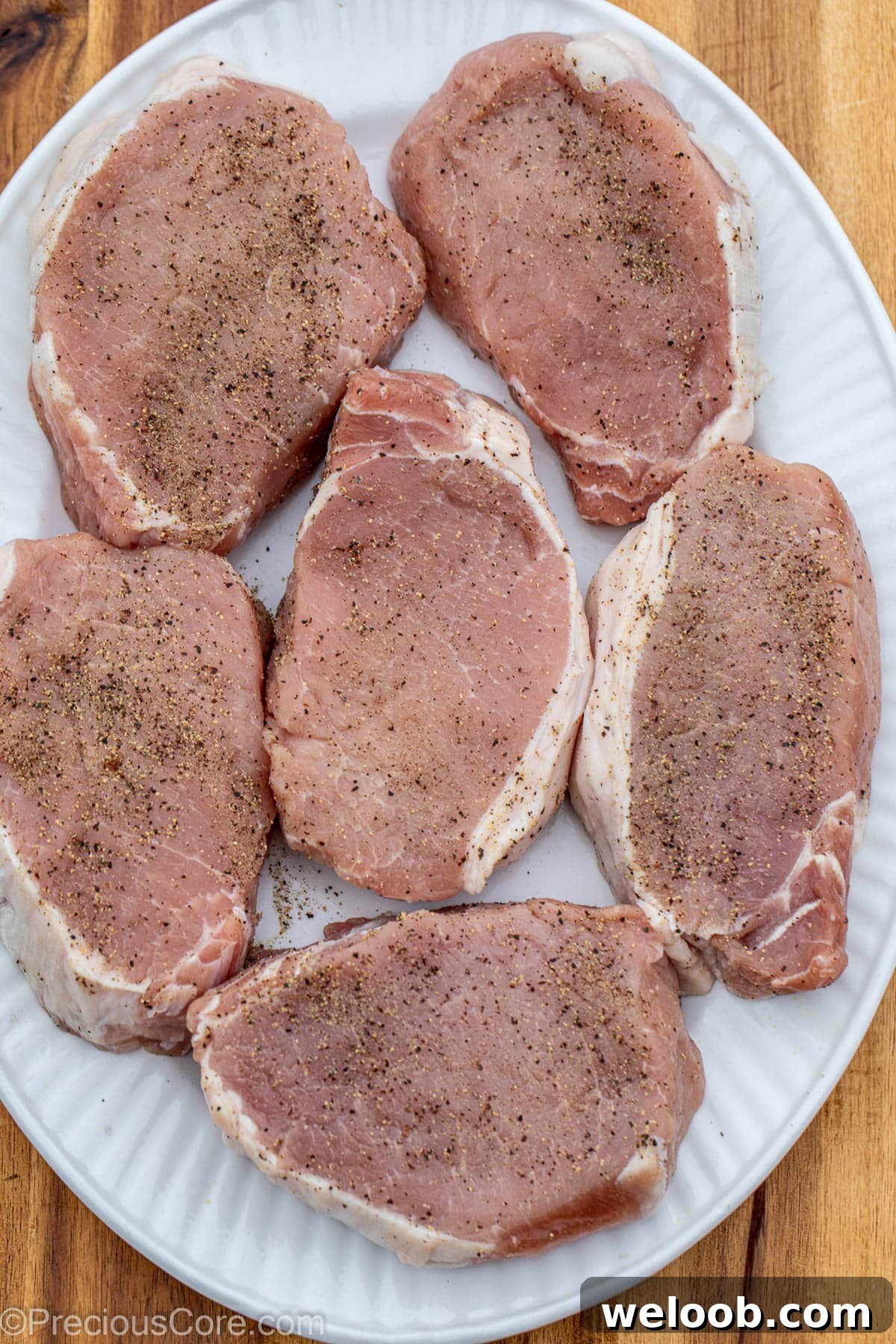 Pork chops in pan, seasoned with salt and pepper.