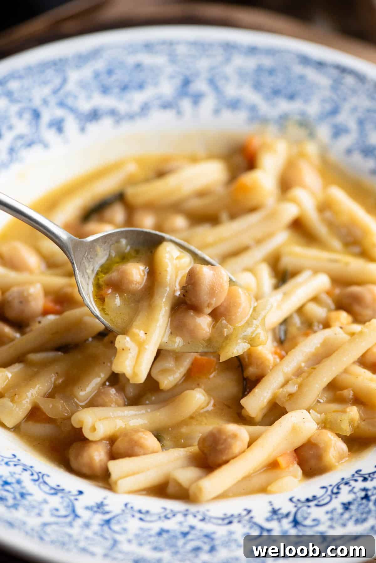 A close up of a spoonful of pasta and chickpeas over a blue bowl.