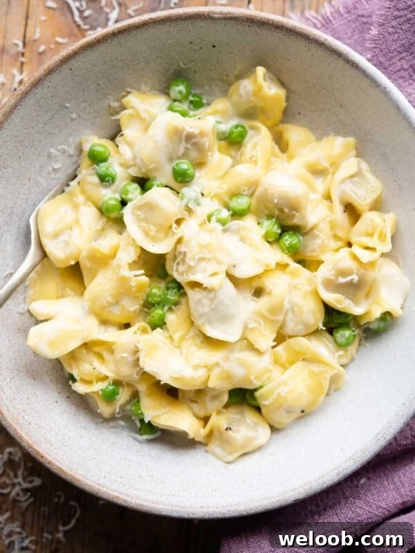 An overhead shot of Tortellini in a bowl with a cream sauce and peas