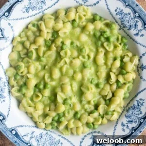 A cropped overhead shot of pasta and peas in a blue patterned bowl.