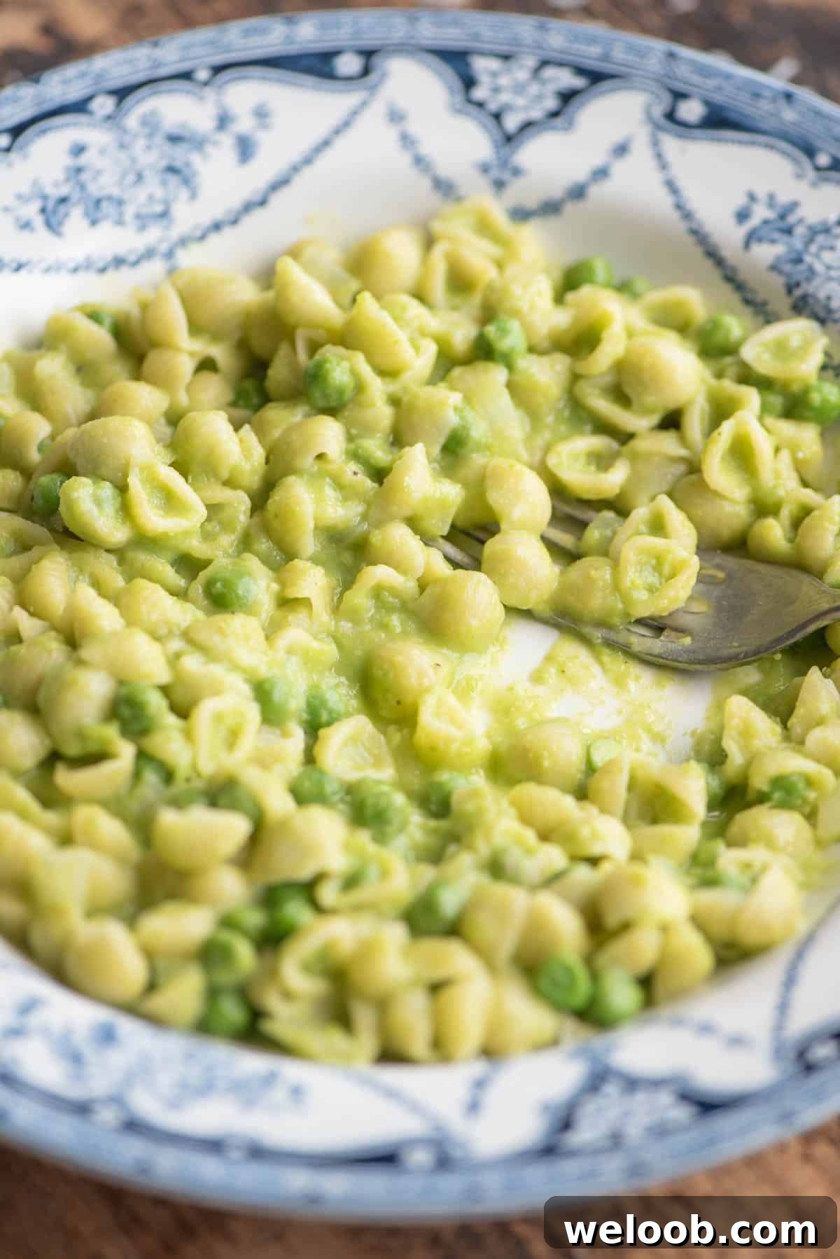 A side shot of pasta and peas in a blue patterned bowl with a fork.